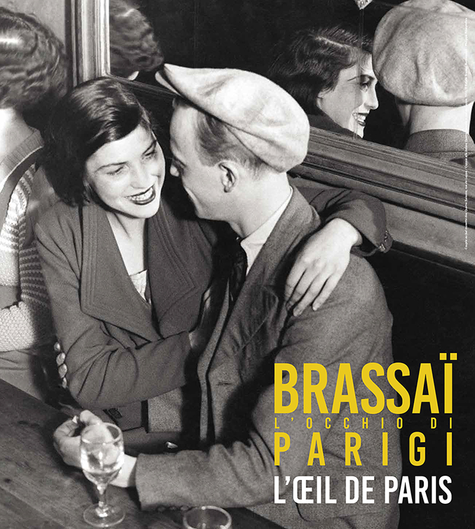 Brassaï, Coppia alla balera Quatre-Saisons in rue de Lappe, 1932 © Estate Brassaï Succession – Philippe Ribeyrolles. Fotografia in bianco e nero di due giovani seduti in un locale pubblico con due bicchieri appoggiati sul tavolo e uno specchio alle loro spalle.