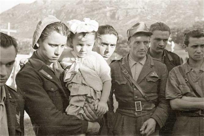 Châtillon (Champ-de-Cort), juin 1945. Exhumation de la dépouille du chef de la bande de la Suelvaz Émile Lexert « Milò » de l’ancien cimetière. Au milieu le partisan Mario Minuzzo « Alpino » avec dans les bras la fille de Milò, Renata Lexert. © Région autonome Vallée d'Aoste - Photo Octave Bérard (fonds Bérard)